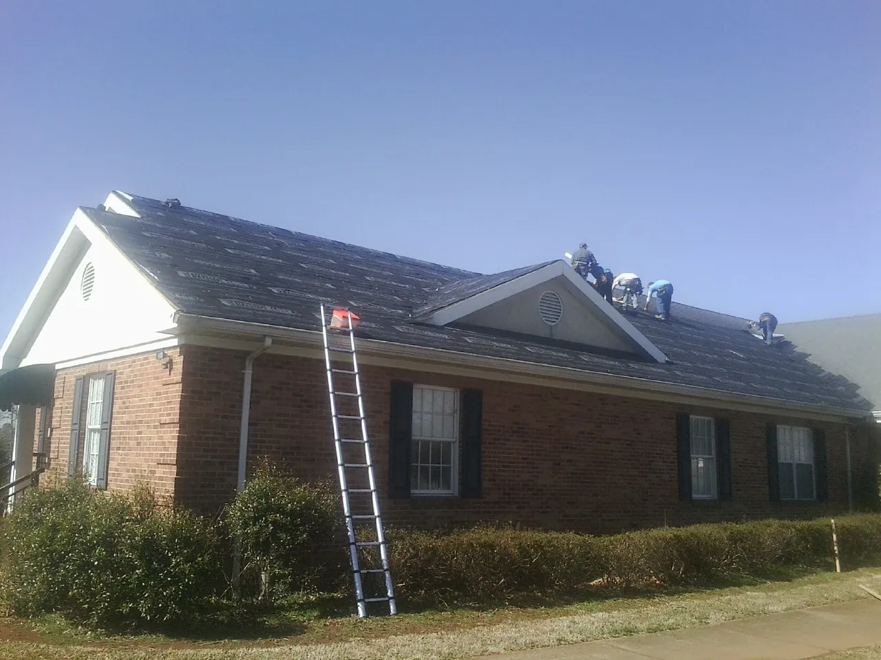 Crew tearing shingles off a brick ranch roof with a ladder set — Metal Roof Repair work by our crew in Port Ewen