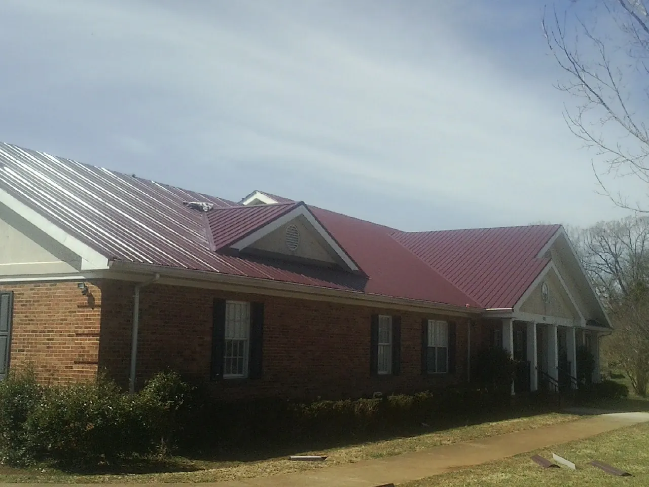 Red metal roof with gabled entries on a long brick building, from a Hail Damage Roof Repair job in Port Ewen