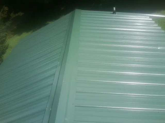 New green metal panels meeting at the ridge of a roof — Flat Roof Repair work by our crew in Port Ewen