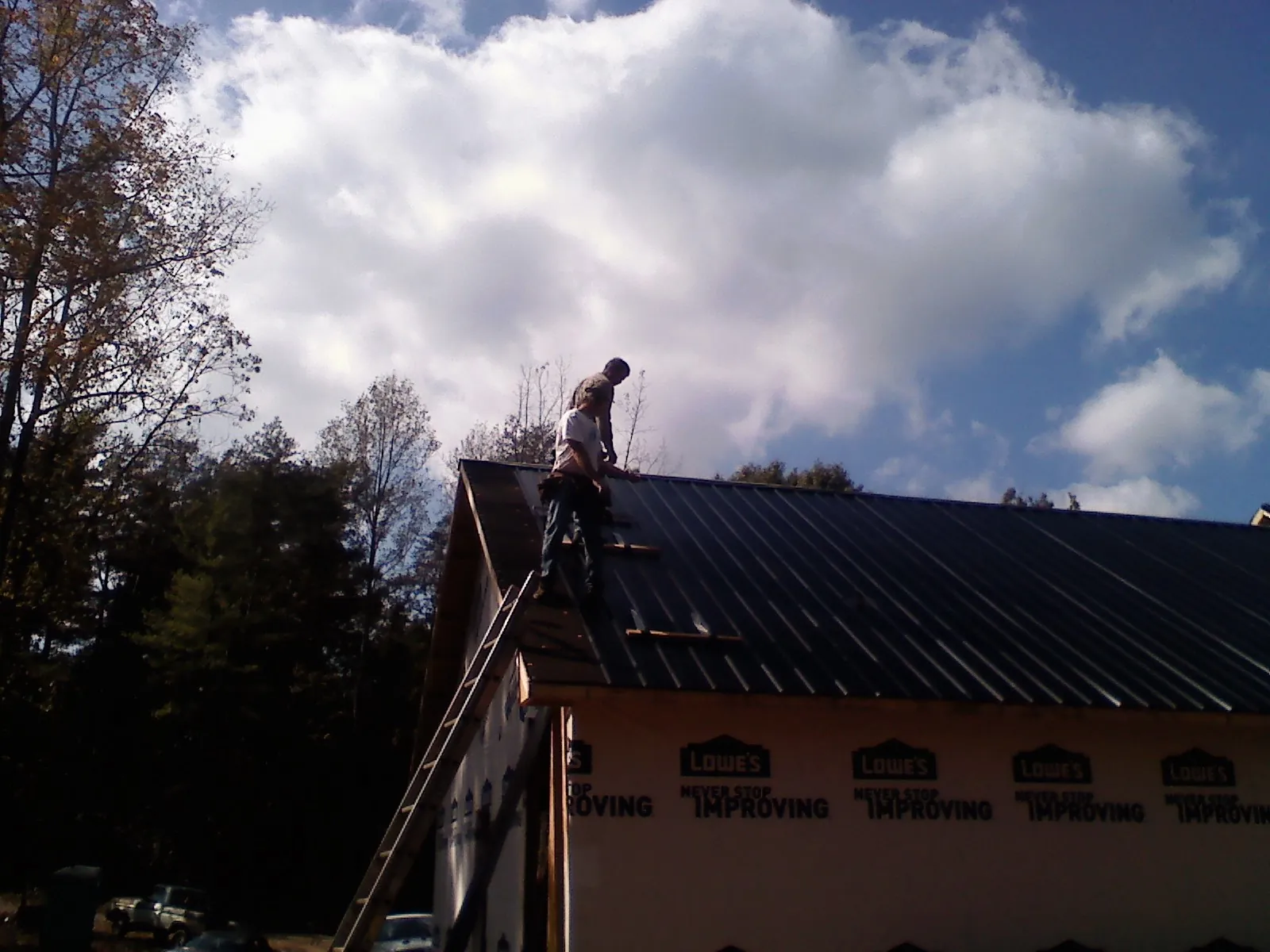 Roofer fastening dark metal panels high against a cloudy sky, from a Roof Inspection job in Port Ewen
