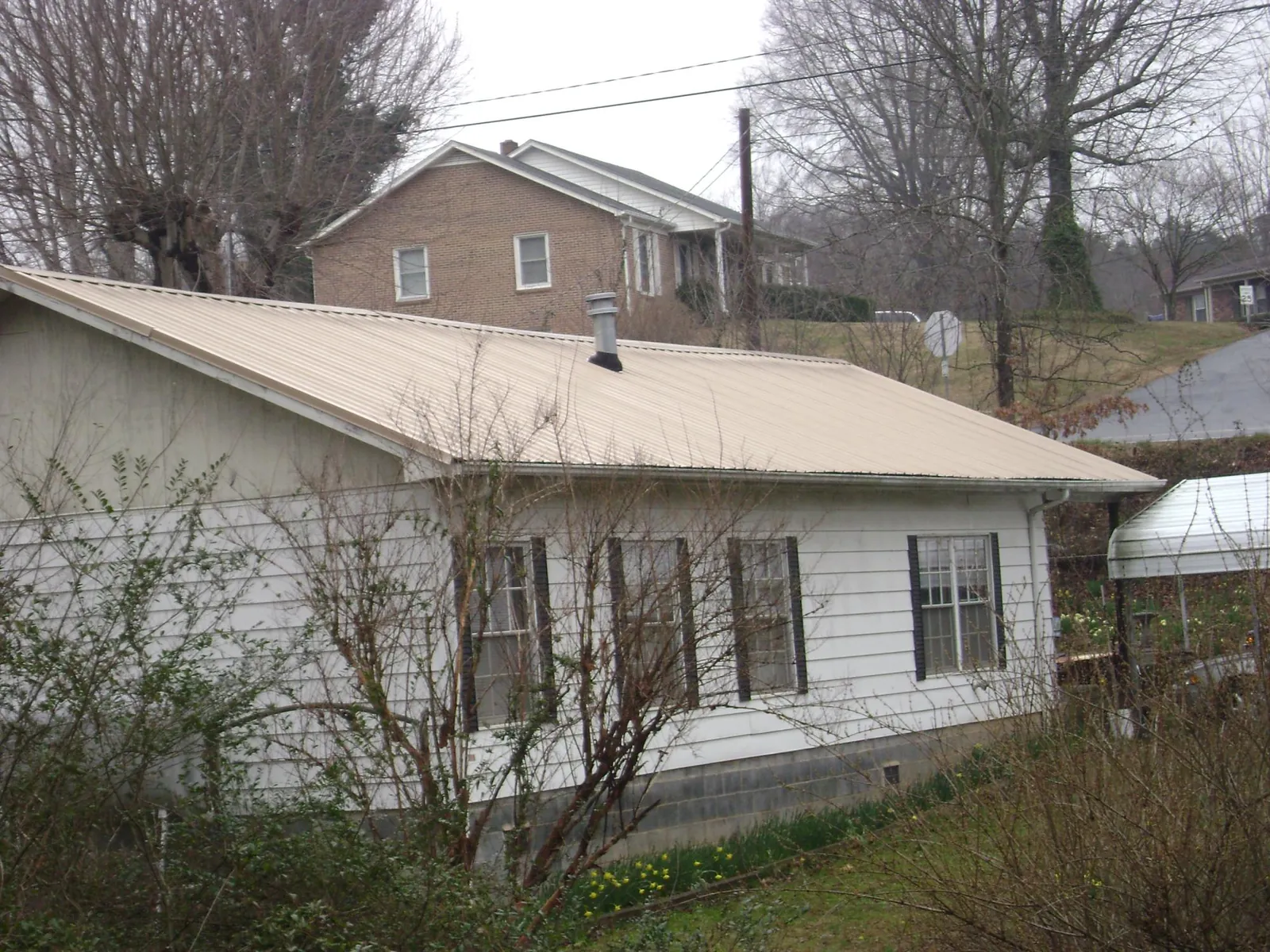 Tan metal roof on a white sided house set into a hillside — Commercial Roofing by Roofing Brothers in Port Ewen
